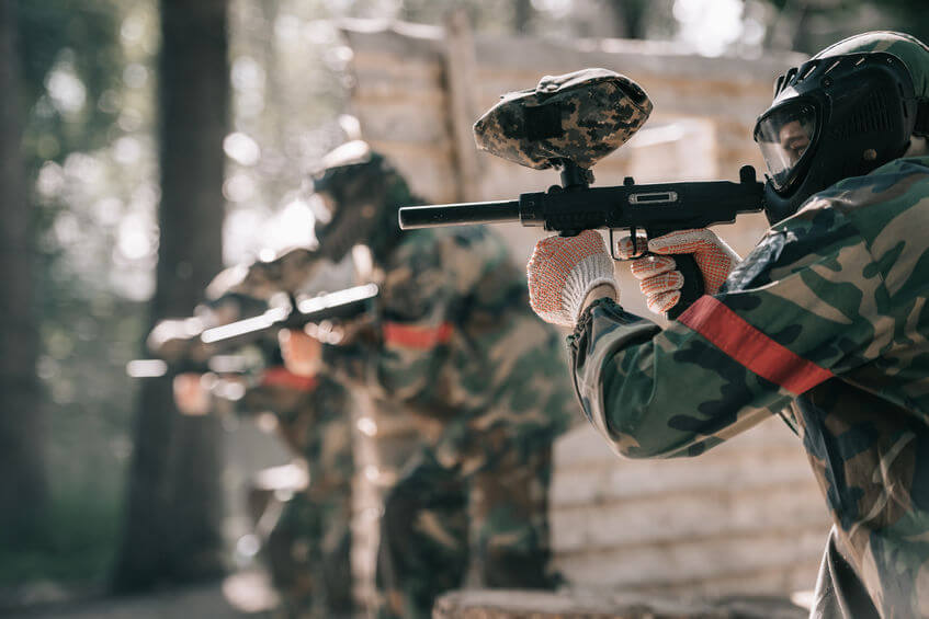 paintball player in goggle mask aiming with marker gun
