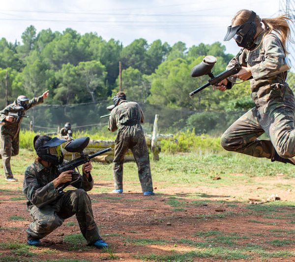 female player jumping and aiming marker on paintball player