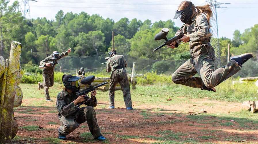 female player jumping and aiming marker on paintball player