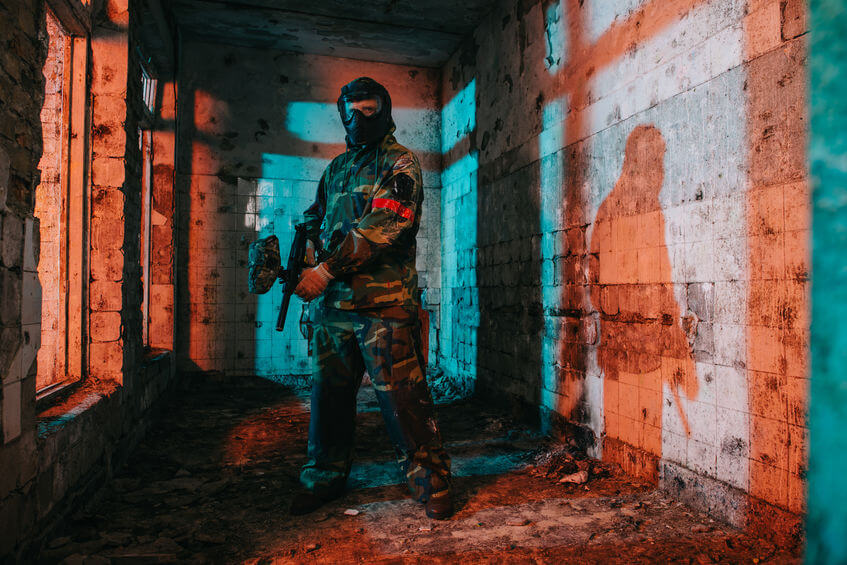 paintball player in goggle mask and camouflage holding paintball gun