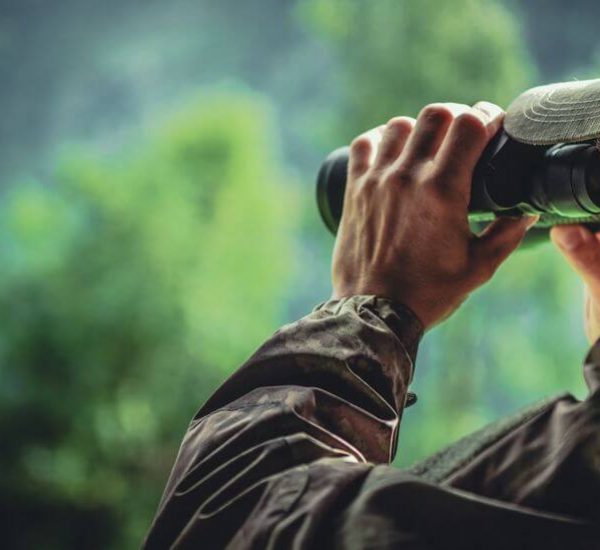 hunter in camouflage with tactical binoculars spotting wildlife