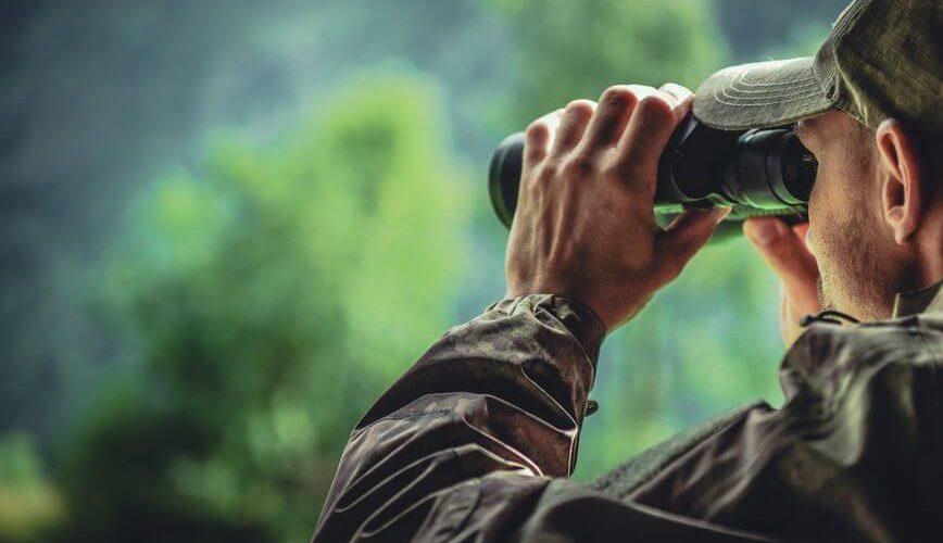 hunter in camouflage with tactical binoculars spotting wildlife