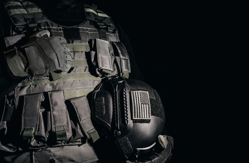 soldier in tactical plate carrier vests standing and holding military helmet