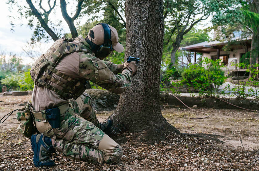 man wearing tactical camouflage and pointing his airsoft pistol