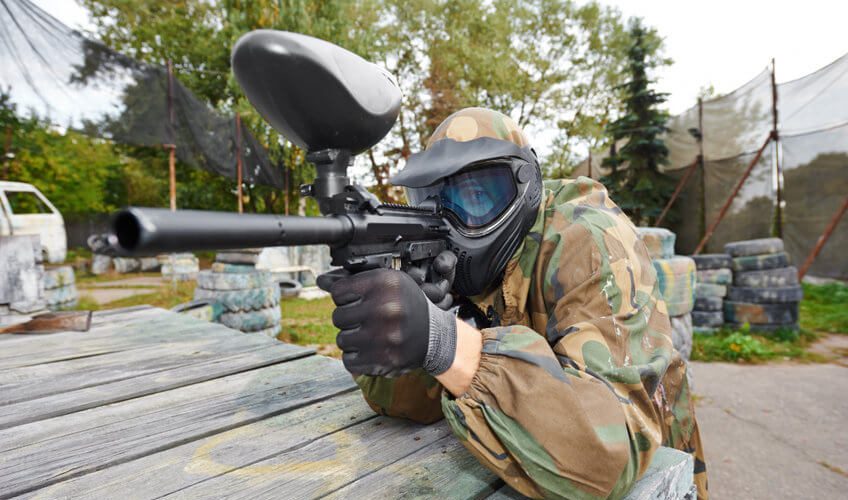 paintball player in protective uniform aiming marker