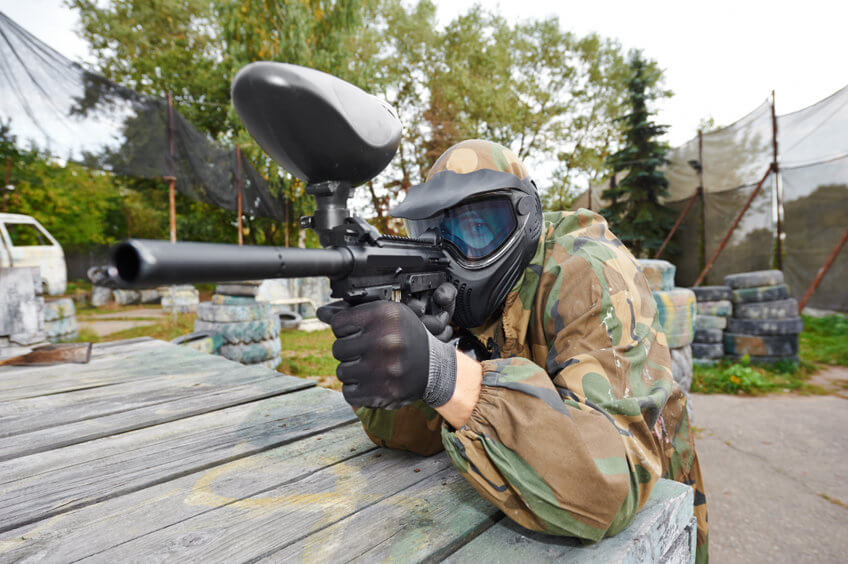 paintball player in protective uniform aiming marker